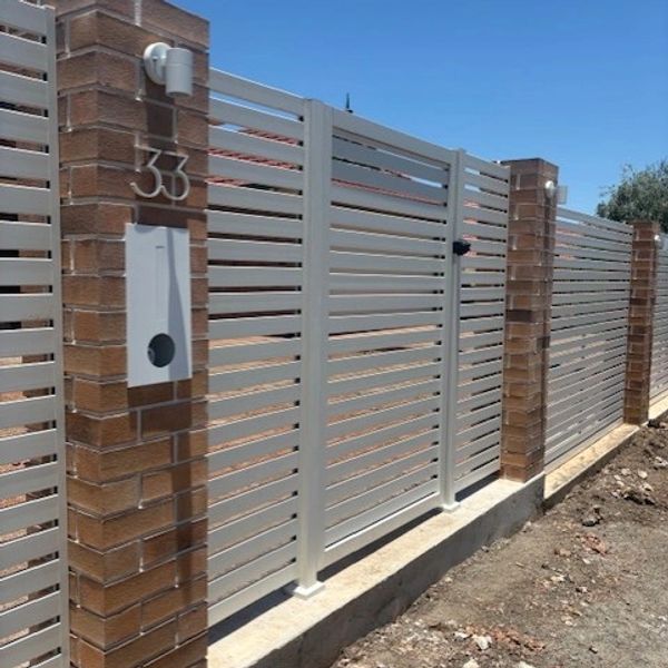 Modern white metal fence with brick pillars under clear blue sky.
