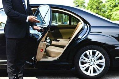 A person opening a car door of a luxury sedan.