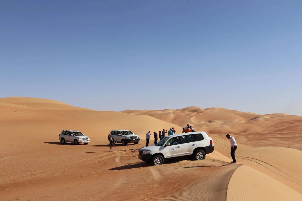 Three SUVs and people in a desert with sand dunes.