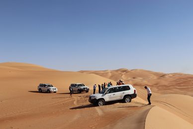 Off-road vehicles navigating desert dunes with people standing around.