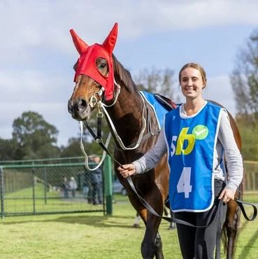 A woman leads a racehorse wearing a red mask and blue vest with number 4.