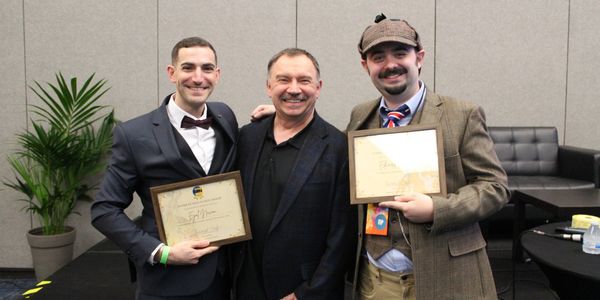 Three men posing with certificates in a formal setting.