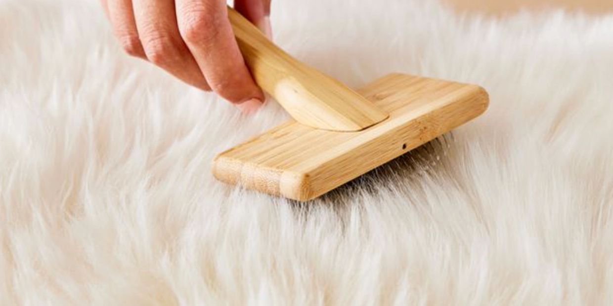 Hand brushing a fluffy white fur rug with a wooden brush.