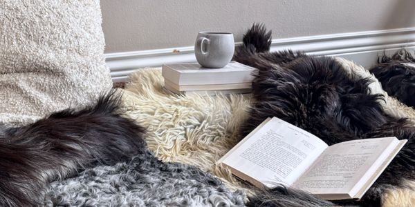 A cozy scene with a black dog resting beside an open book and a cup on a fluffy surface.