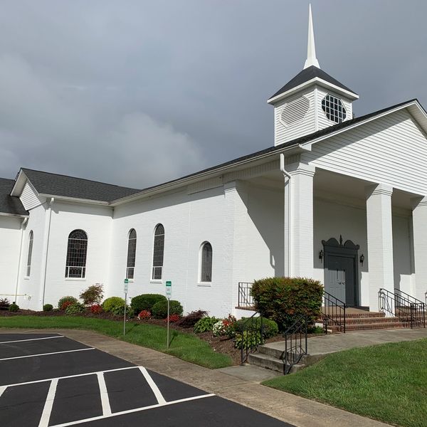 White church with a tall steeple under a cloudy sky.