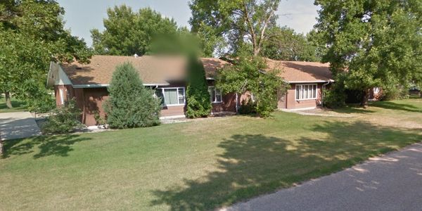 Single-story brick house with a large green lawn and mature trees.