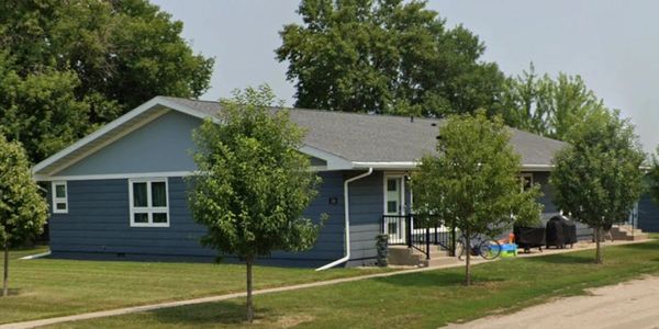 Single-story blue house with small trees in front and a sidewalk.