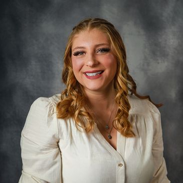 Smiling woman with curled hair wearing a cream blouse and jeans.