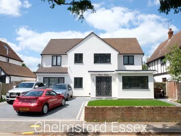 A modern white two-story house with a tiled roof and driveway with cars.