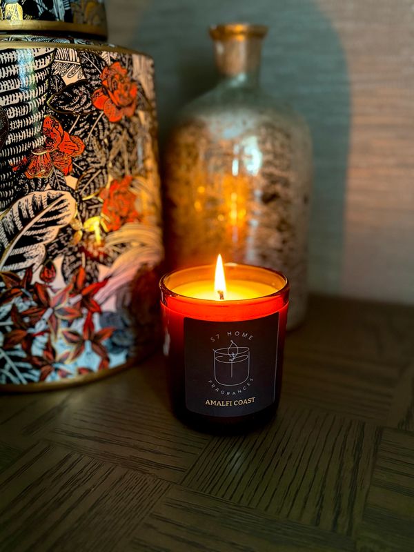 Lit Amalfi Coast scented candle beside decorative vases on a wooden surface.
