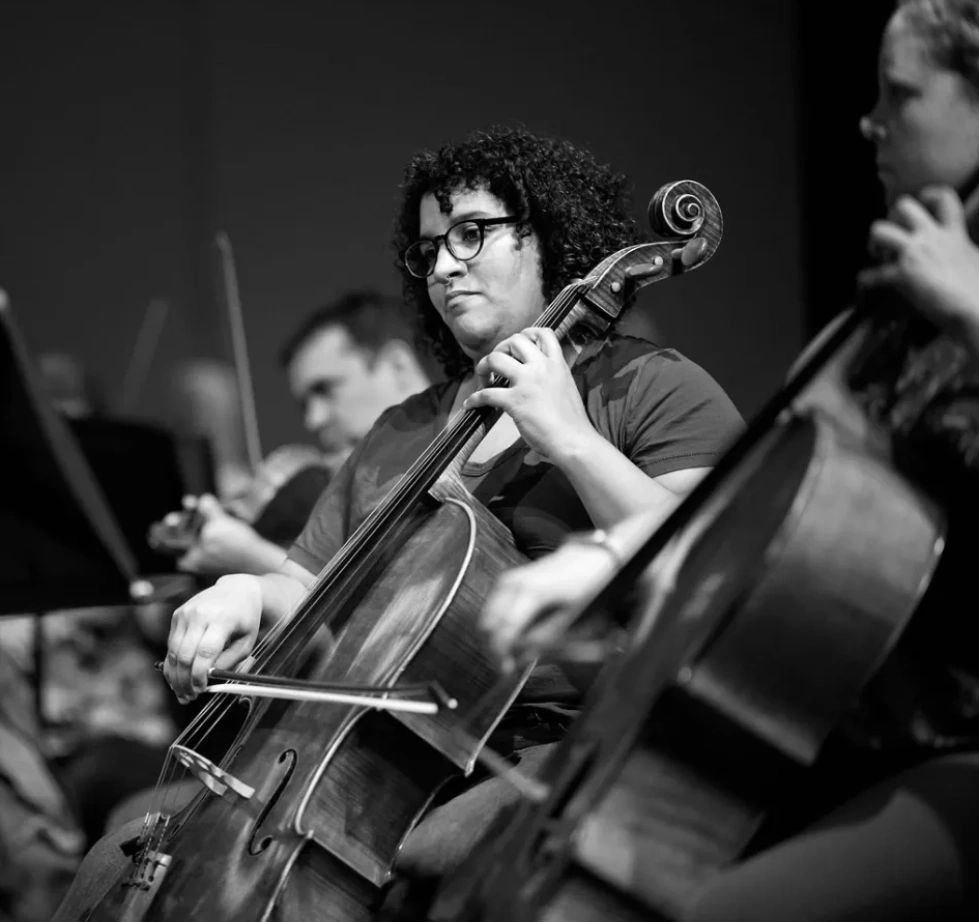 Image of two players in the cello section. You can see a few viola players in the background.