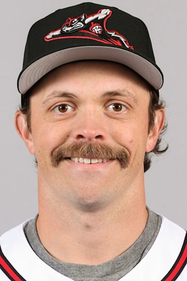 Smiling man wearing a black baseball cap and sports jersey.