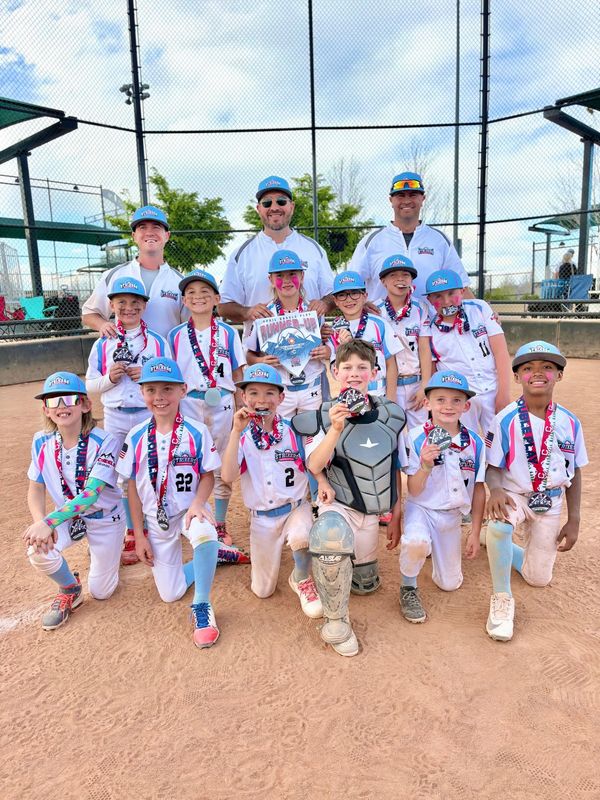 Youth baseball team posing with medals and trophy after a game.