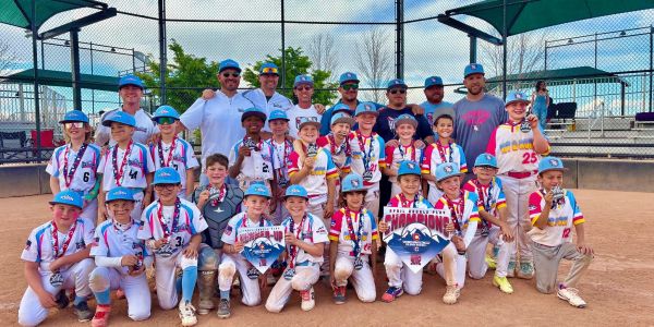Youth baseball team posing on field with medals and championship signs.