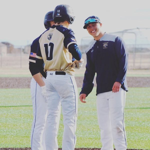 Three baseball players in uniform smiling and conversing on the field.