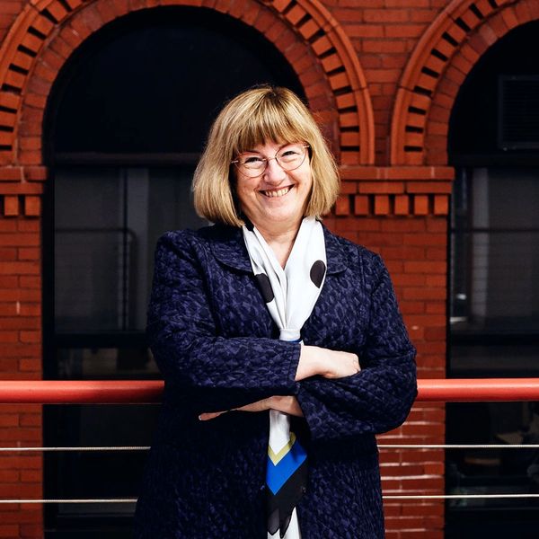 Smiling woman, financial consultant Susan Goodison, in front of a brick building in a blue jacket.