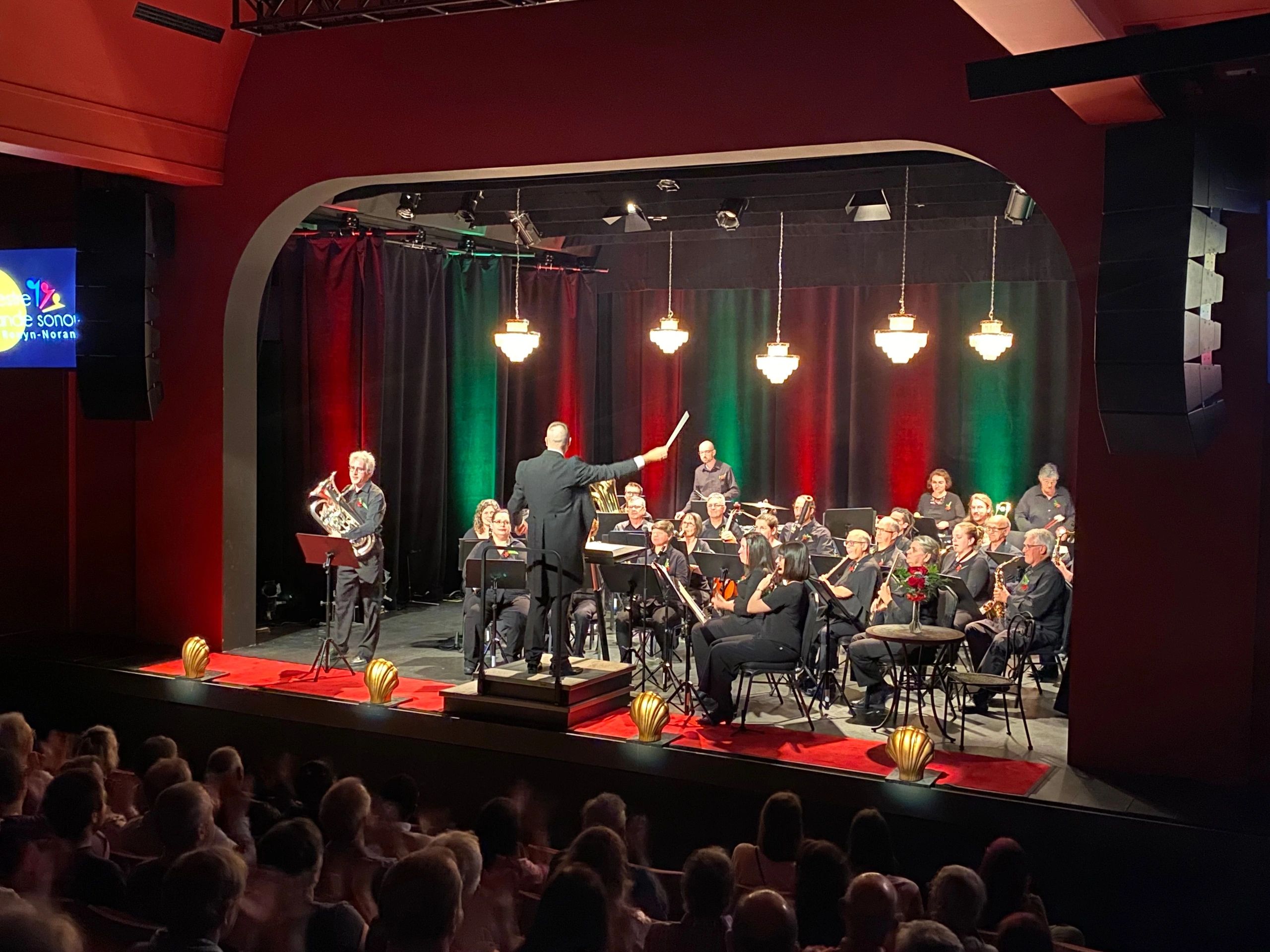 Conductor leading a band performance on stage with audience watching.
