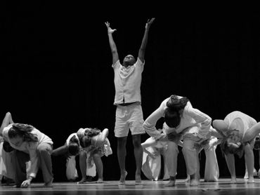 A group of dancers performing, one standing with arms raised.