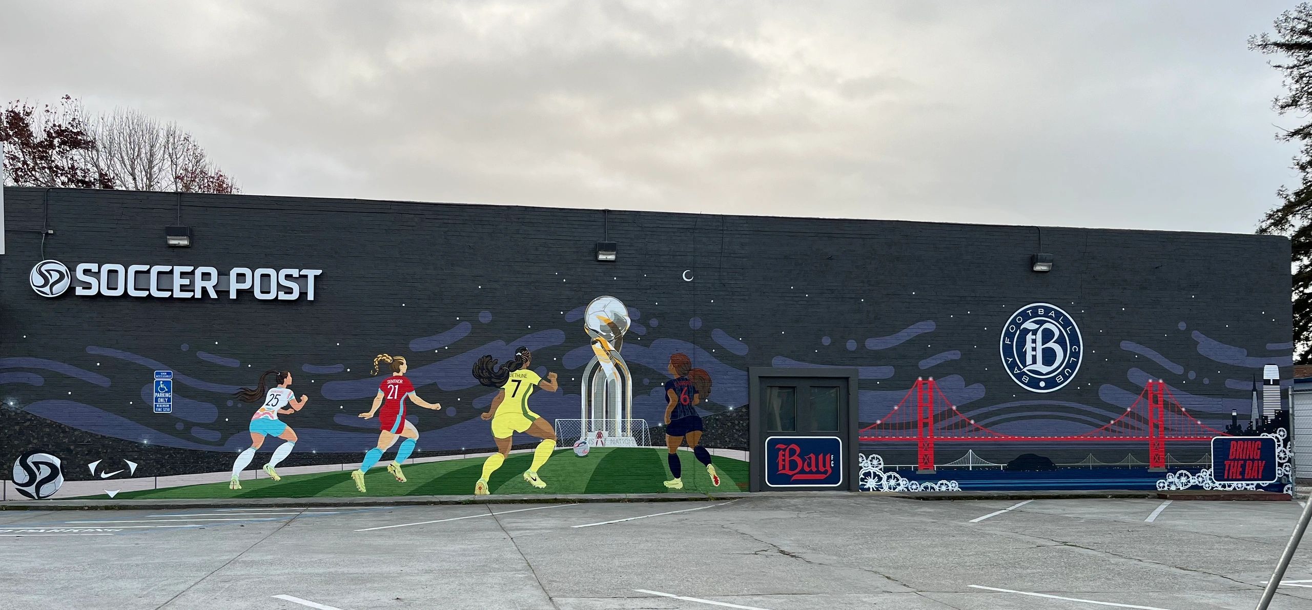 Mural of women soccer players, trophy, and Golden Gate Bridge on a building.
