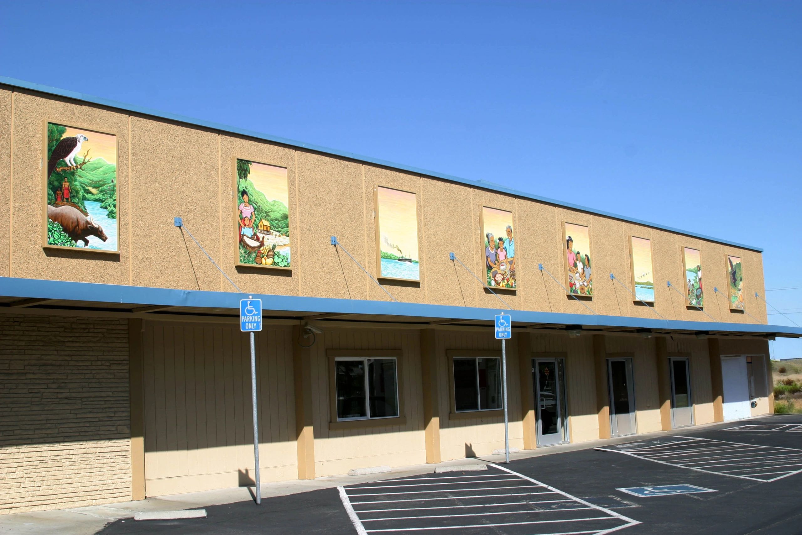 Mural paintings depicting nature and community on a beige building under clear blue sky.