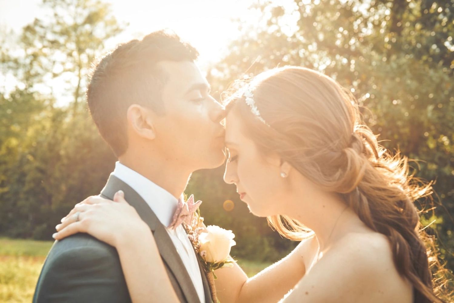 Groom kissing bride on forehead after wedding on natural, native Texas property with light streaming