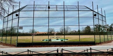 Empty baseball field behind protective netting on a clear day.
