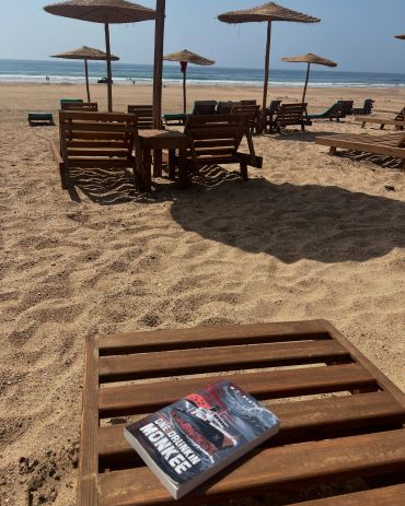Book and chairs on a sandy beach with umbrellas.
