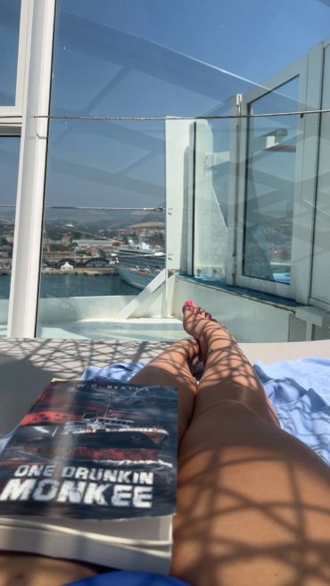 Person relaxing on a deck with a book under sunlight.
