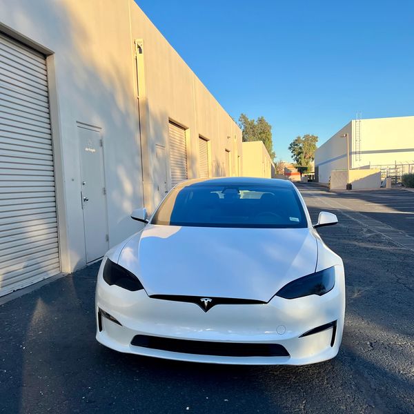 Front view of a white Tesla Model S parked outside industrial buildings.
