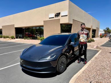 Man standing next to a black Tesla car in a parking lot.