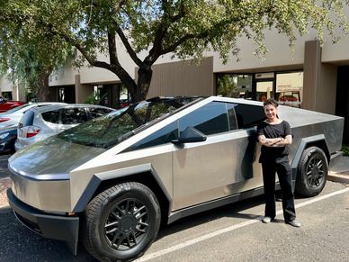 Man standing beside a Tesla Cybertruck in a parking lot.