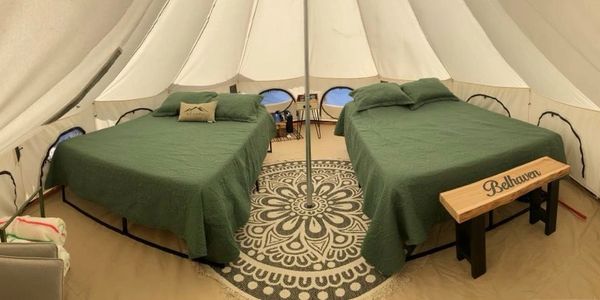 Two green-covered beds inside a spacious, well-lit tent with a decorative rug.