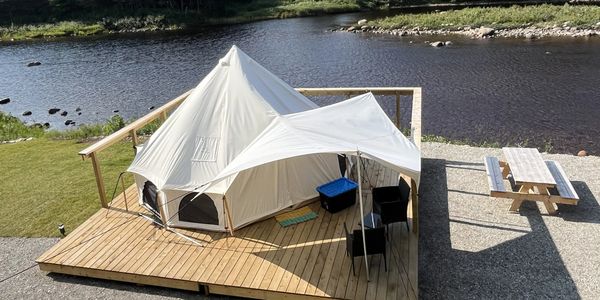 A white tent set up on a wooden platform beside a river with chairs and a picnic table.