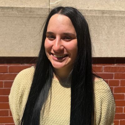 Smiling woman with long black hair in a knitted beige sweater.