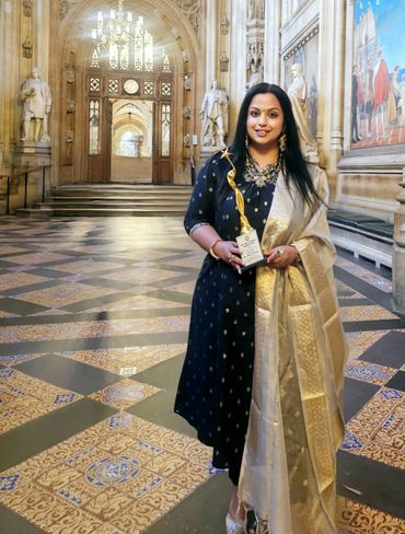 Woman in traditional attire holding an award in a grand hall.