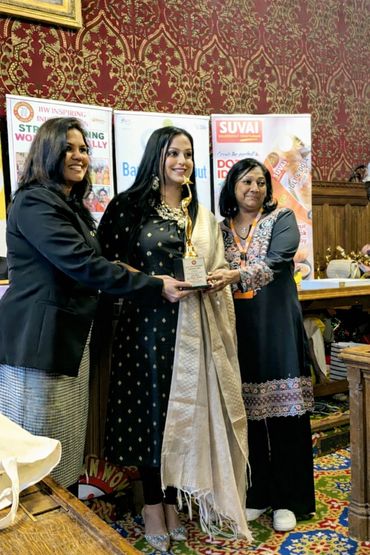 Three women stand together, one holding a trophy, smiling in a formal setting.