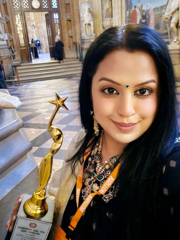 A woman proudly holding a golden award trophy inside an ornate building.