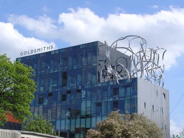 Modern Goldsmiths building with artistic metal sculpture on roof under blue sky.
