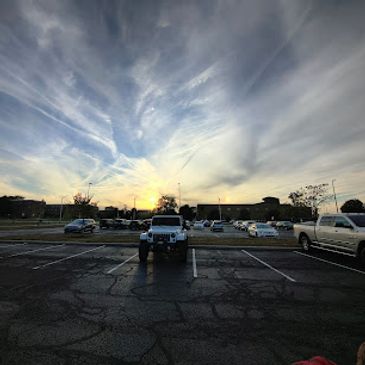 Sunset over a parking lot with scattered cars and dramatic clouds.