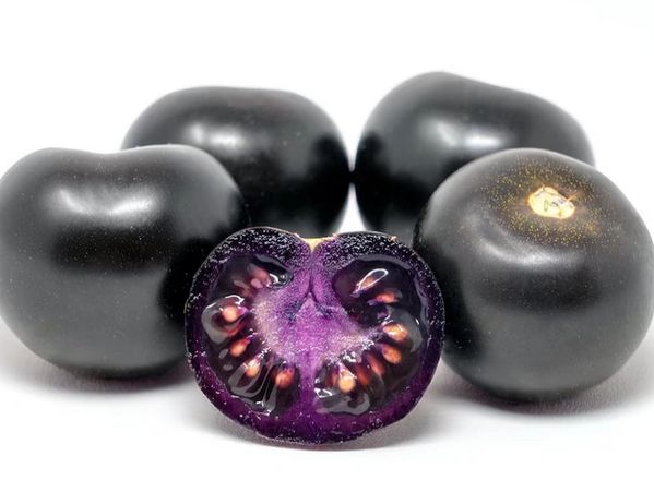Close-up of black tomatoes with one cut in half showing purple interior and seeds.