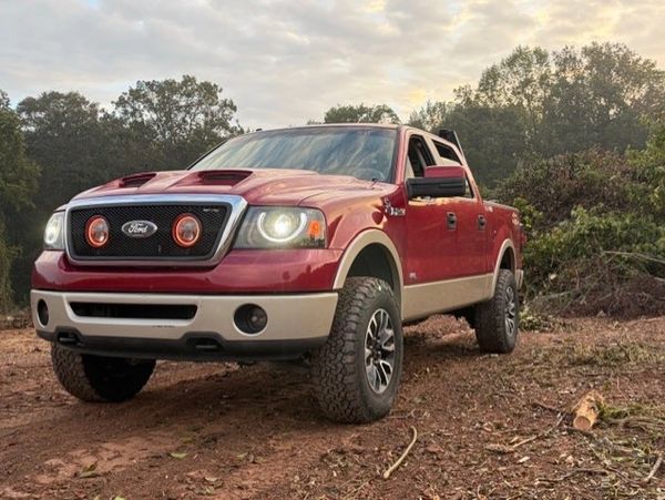 Red Ford pickup truck parked on a dirt trail at sunset.