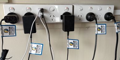Multiple power cords plugged into wall sockets with test tags.