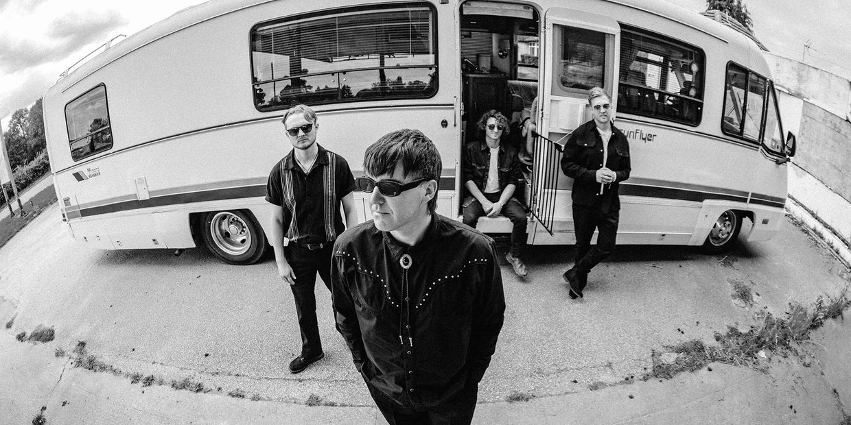 Black and white photo of four men near a camper van.