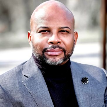 Confident man in a gray blazer and black turtleneck.