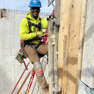 Construction worker smiling on site wearing safety gear.