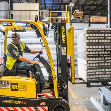Forklift operator moves stacked pallets in a warehouse.