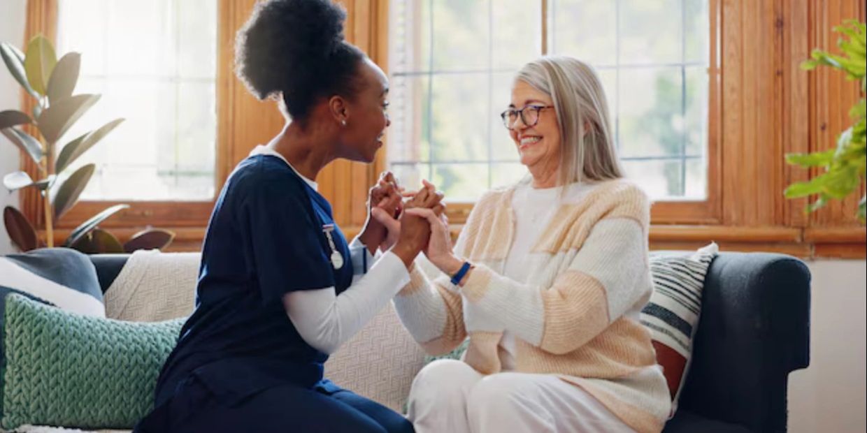 Nurse and elderly woman share a joyful moment on a couch.