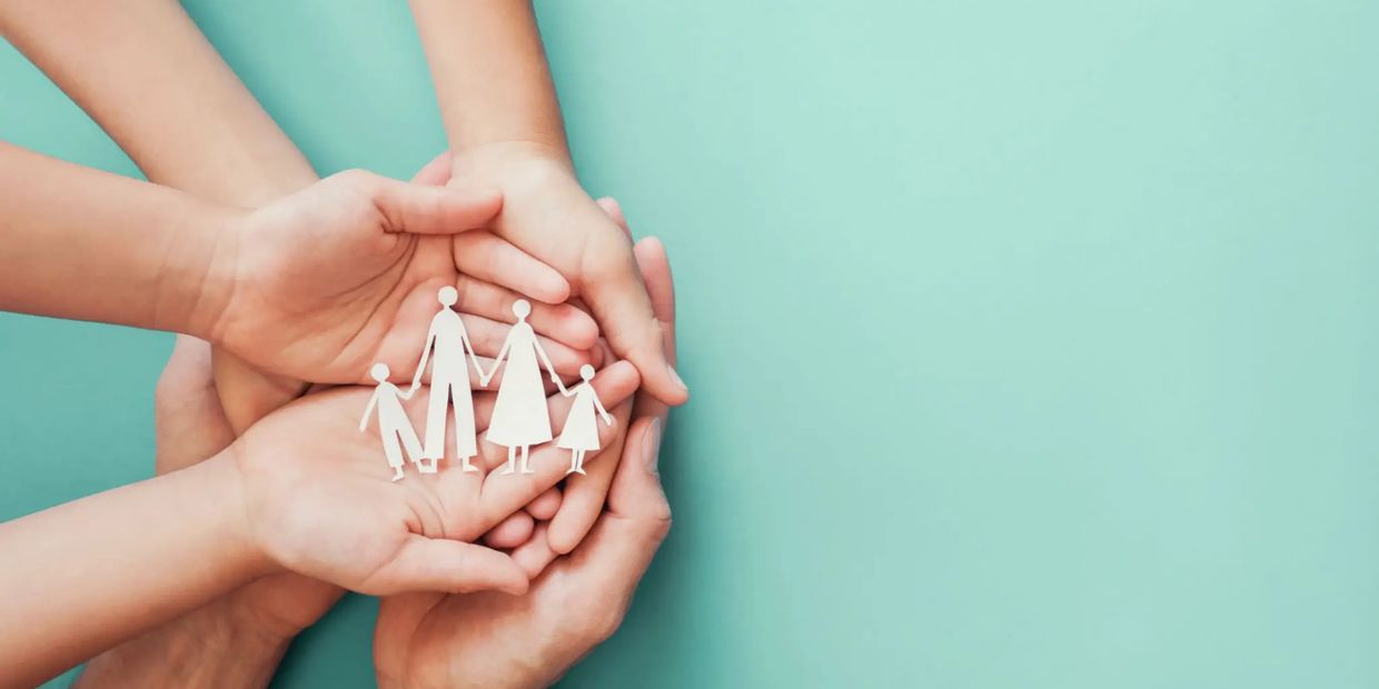 Hands holding paper cutout of family figures symbolizing care and protection.