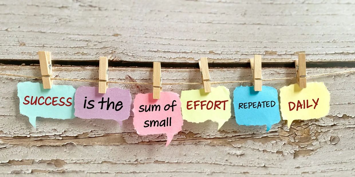 Colorful notes with a motivational quote clipped on a string against a rustic wooden background.