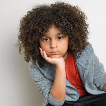 Thoughtful child with curly hair resting chin on hand.